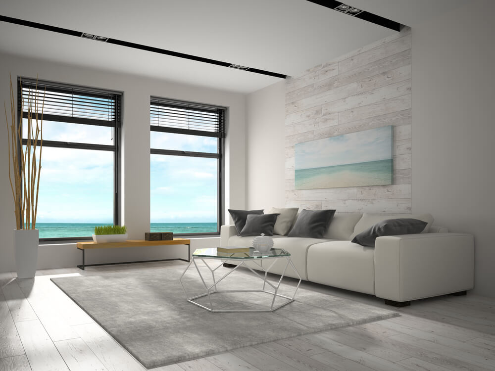Modern coastal living room featuring dark-framed impact windows with an ocean view, installed by STS Impact Windows & Doors.